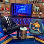 man, toddler, child, studio, television, chair, carpet, bookshelf, book, suit, tie, yellow_shirt, denim_shorts, modern, decor, smile, indoors, table, show, colorful