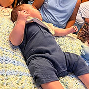 Cj is registered to the contest to win money with this photo: baby, infant, blanket, crochet, blue_clothing, bib, person, adult, smile, indoor, furniture, table, cup, relaxation, family, home, casual, sitting, comfort, soft_texture