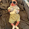 Cj is registered to the contest to win money with this photo: baby, infant, sunglasses, mittens, blanket, clothing, socks, person, cute, newborn, lying_down, indoors, soft, cozy, fashion, accessories, relaxing, portrait, small, child