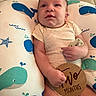 baby, infant, cushion, whale_pattern, wooden_sign, pacifier, clothing, lying_down, cute, child, person, skin, face, hand, expression, indoor, soft_lighting, newborn, milestone, background