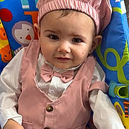 Saige joined the competition — help win amazing prizes! baby, child, infant, pink_outfit, chef_hat, bow_tie, baby_seat, colorful, animal_print, cute, smiling, portrait, sitting, indoors, clothing, face, person, young_child, happy, comfortable
