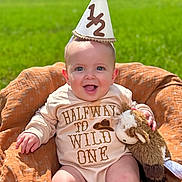 Cyle joined the competition — help win amazing prizes! baby, infant, smiling, party_hat, outdoor, green_grass, stuffed_animal, blanket, clothing, happy, portrait, sitting, cute, headwear, child, nature, sunlight, one_half, toy, celebration