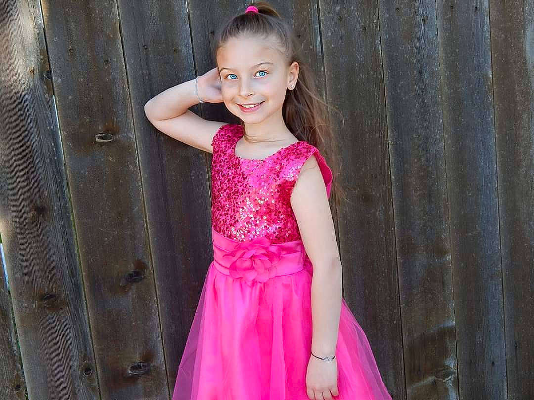 Sarah is registered to the contest to win money with this photo: day_dress, dress, embellishment, eye, face, flash_photography, hair, happy, head, human_body, iris, joy, neck, one_piece_garment, person, pink, purple, skin, sleeve, smile