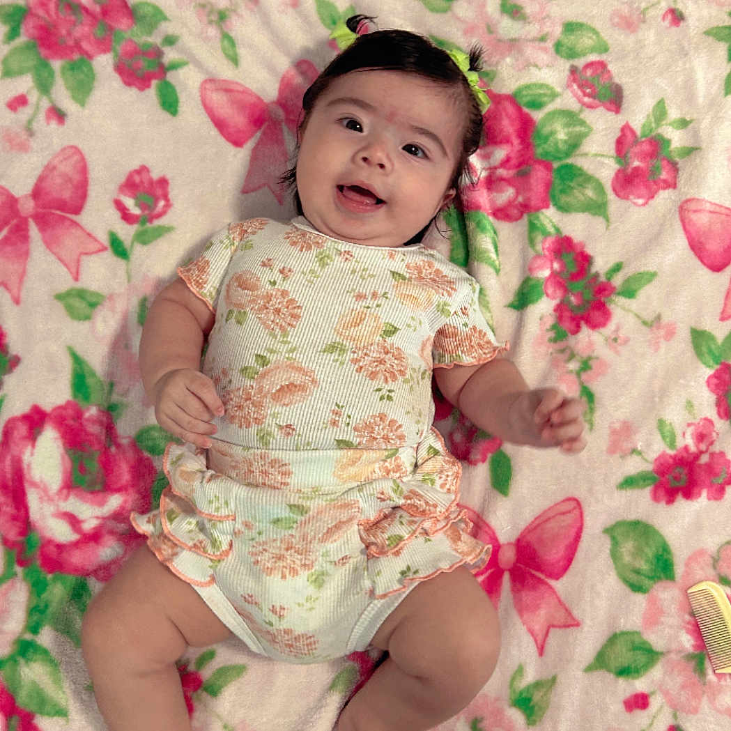 Jenevieve is registered to the contest to win money with this photo: baby, blanket, child, colorful, comfort, cute, face, feet, floral_pattern, hair_ties, hands, happy, indoors, infant, legs, lying_down, onesie, skin, smiling, soft_texture