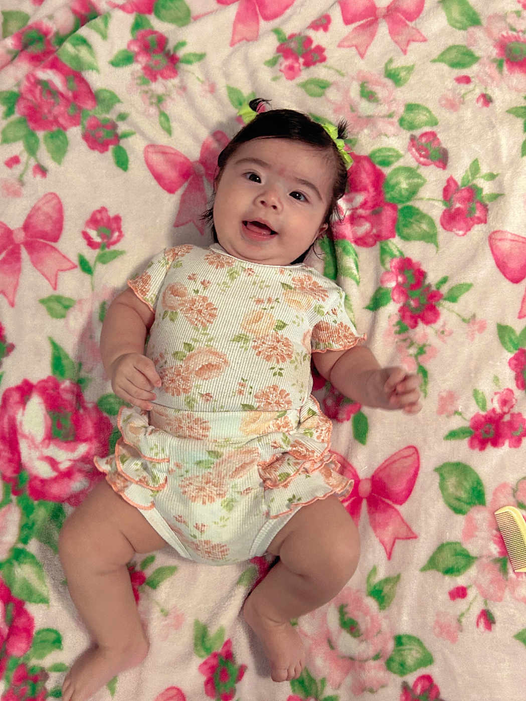 Jenevieve is registered to the contest to win money with this photo: baby, infant, child, smiling, lying_down, floral_pattern, blanket, onesie, hair_ties, cute, happy, skin, face, hands, legs, feet, indoors, soft_texture, colorful, comfort