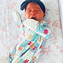 baby, sleeping, yawning, headband, onesie, floral_pattern, infant, cute, bed, blanket, soft, newborn, child, sleepwear, hand, mouth, face, lying_down, pastel_colors, cozy
