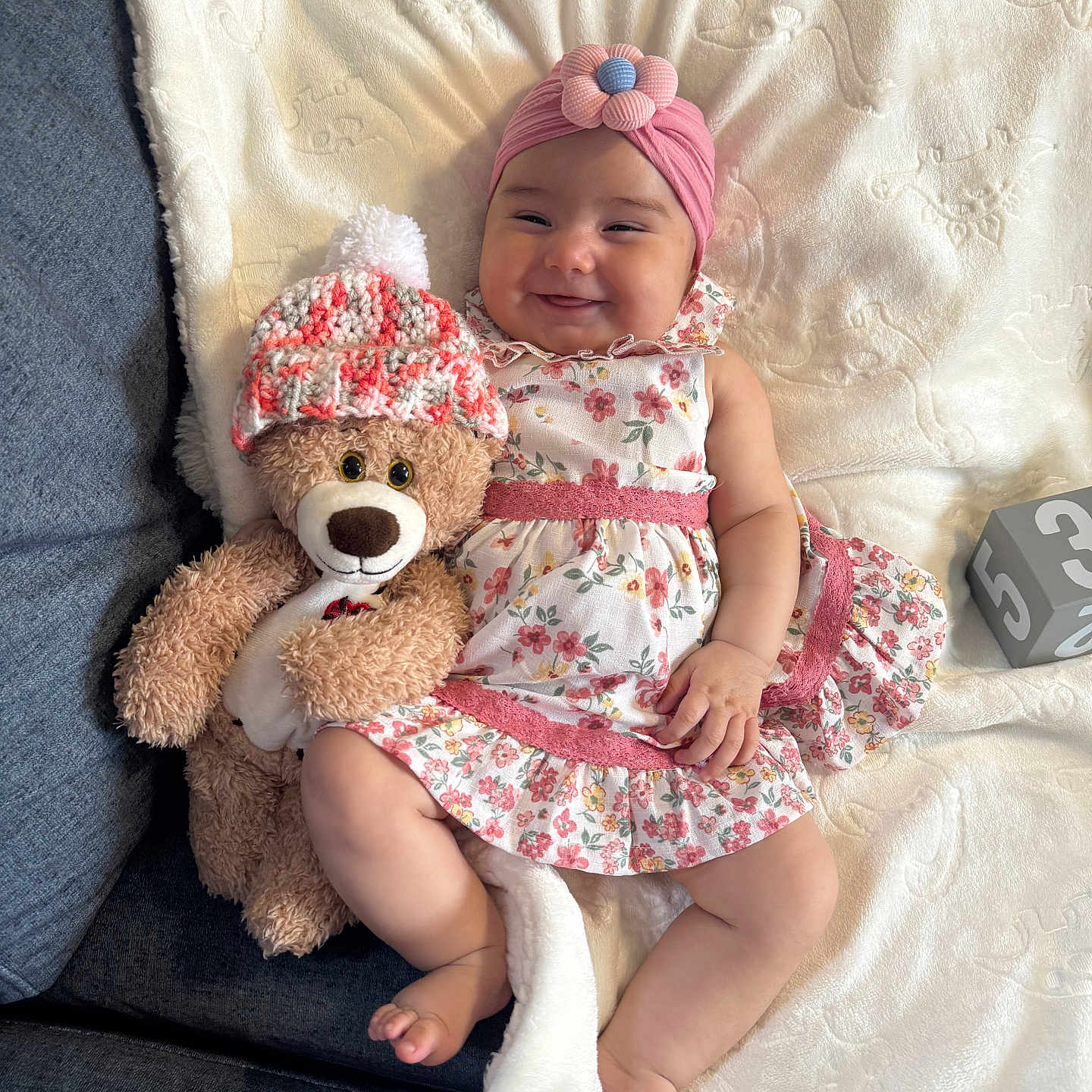 Daniela joined the competition — help win amazing prizes! baby, blanket, child, comfort, couch, cozy, cute, floral_dress, flower, happy, headband, indoors, infant, lying_down, pink, smiling, soft_texture, stuffed_animal, teddy_bear, toy