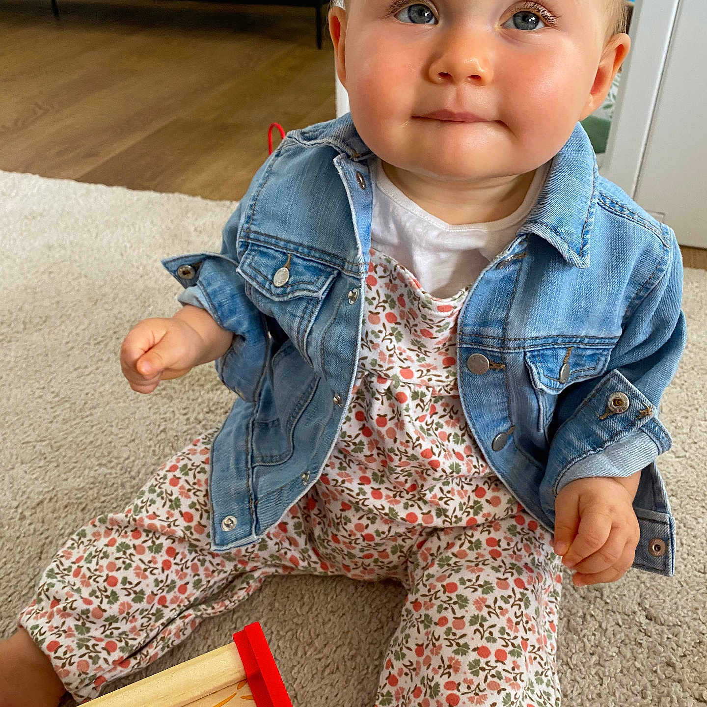 Sixtine a rejoint le concours — aidez-le/la à gagner de superbes lots ! adorable, baby, blue_eyes, carpet, child, clothing, curious, cute, denim_jacket, expression, face, floor, floral_outfit, hands, indoor, infant, person, playful, sitting, wooden_toy