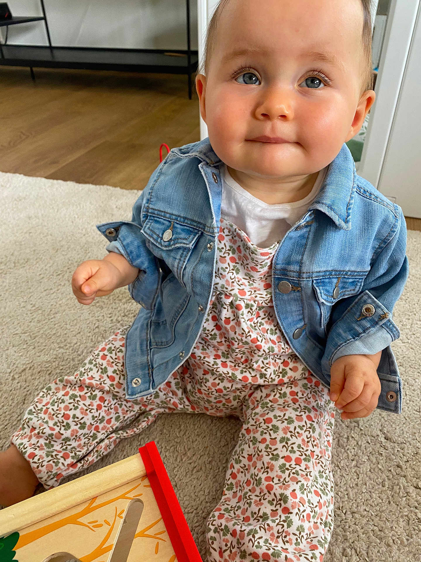 Sixtine a rejoint le concours — aidez-le/la à gagner de superbes lots ! baby, child, denim_jacket, floral_outfit, carpet, wooden_toy, indoor, cute, blue_eyes, curious, sitting, playful, adorable, infant, hands, face, expression, clothing, floor, person