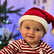 Nail a rejoint le concours — aidez-le/la à gagner de superbes lots ! baby, child, smiling, face, santa_hat, striped_clothing, holiday, christmas_tree, festive, indoors, portrait, cute, happy, person, headwear, red, white, blurred_background, celebration, seasonal