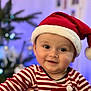 baby, child, smiling, face, santa_hat, striped_clothing, holiday, christmas_tree, festive, indoors, portrait, cute, happy, person, headwear, red, white, blurred_background, celebration, seasonal