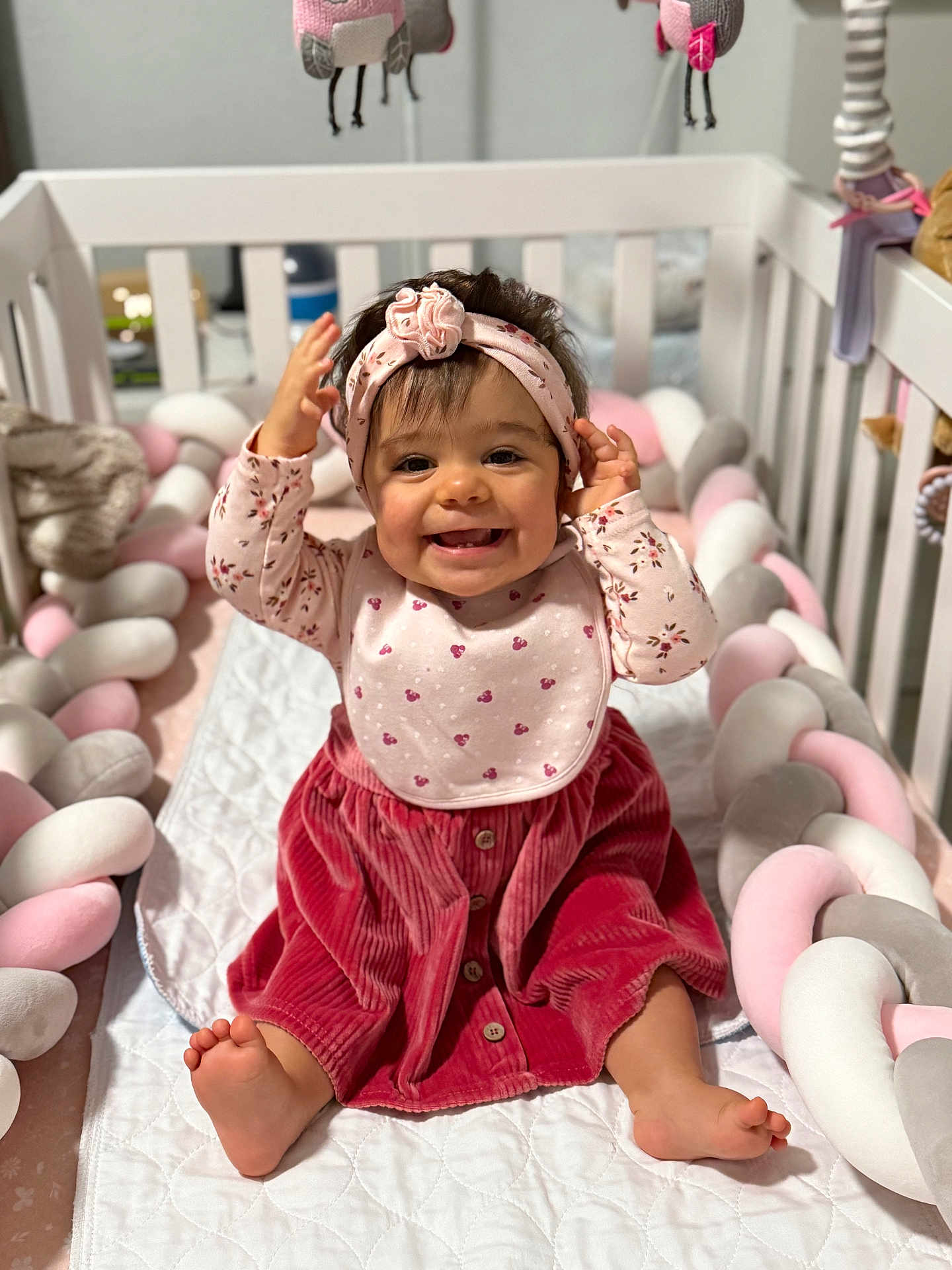 Amaya is registered to the contest to win money with this photo: baby, child, smile, crib, headband, bib, dress, corduroy, pink, red, pastel, braided_cushion, soft_toy, happy, sitting, indoors, cute, infant, portrait, playful