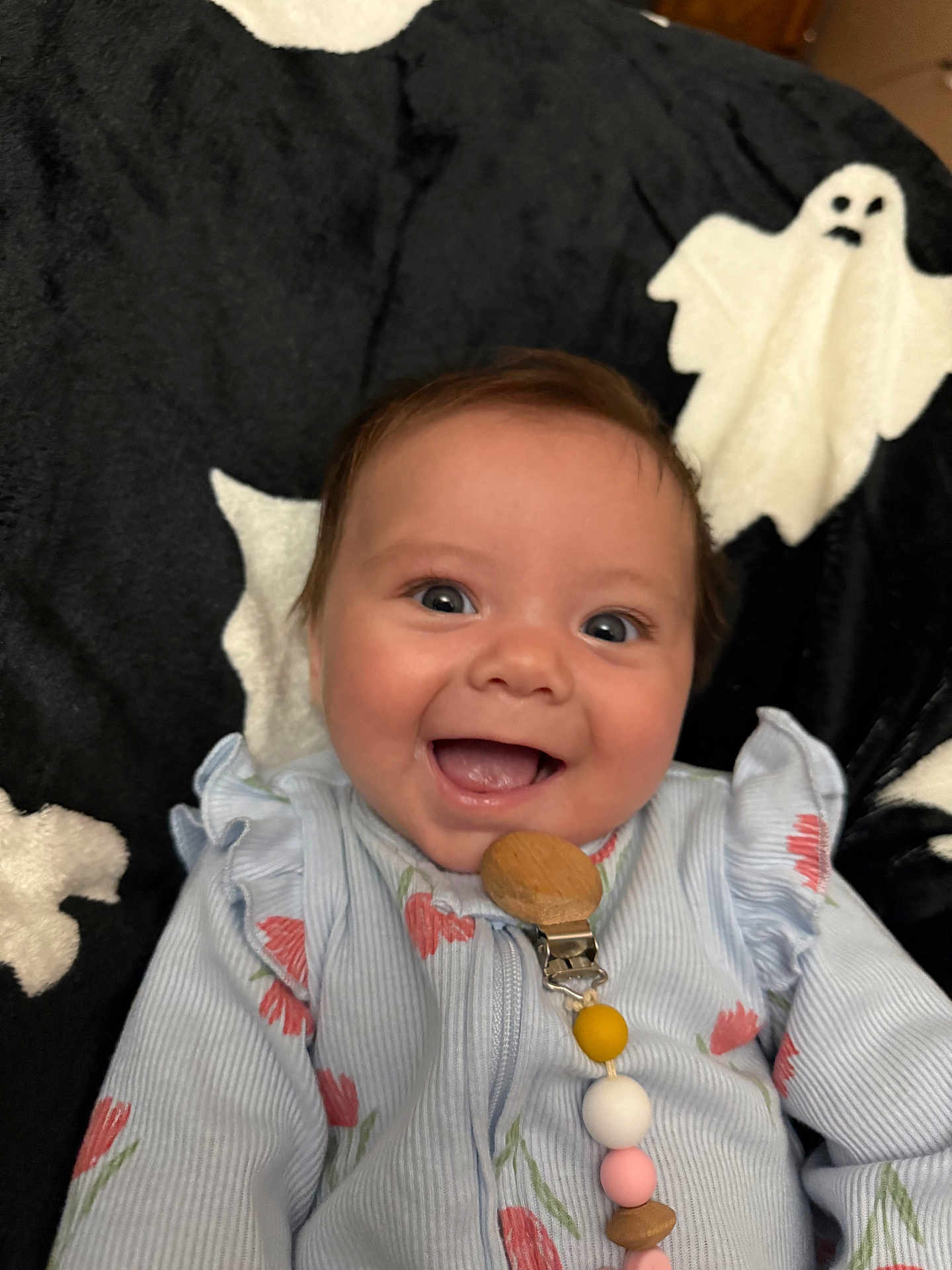 Abriela is registered to the contest to win money with this photo: baby, smiling, infant, pacifier_clip, blue_clothing, floral_pattern, blanket, ghost_pattern, happy, face, cute, child, indoors, closeup, young, person, portrait, comfort, soft_texture, clothing