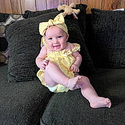 Lilith Fae Deatley joined the competition — help win amazing prizes! baby, smiling, yellow_outfit, headband, couch, plush_toy, wood_paneling, happy, infant, child, indoors, cute, sitting, person, furniture, cheerful, playful, young_child, cozy, portrait