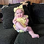 baby, smiling, yellow_outfit, headband, couch, plush_toy, wood_paneling, happy, infant, child, indoors, cute, sitting, person, furniture, cheerful, playful, young_child, cozy, portrait