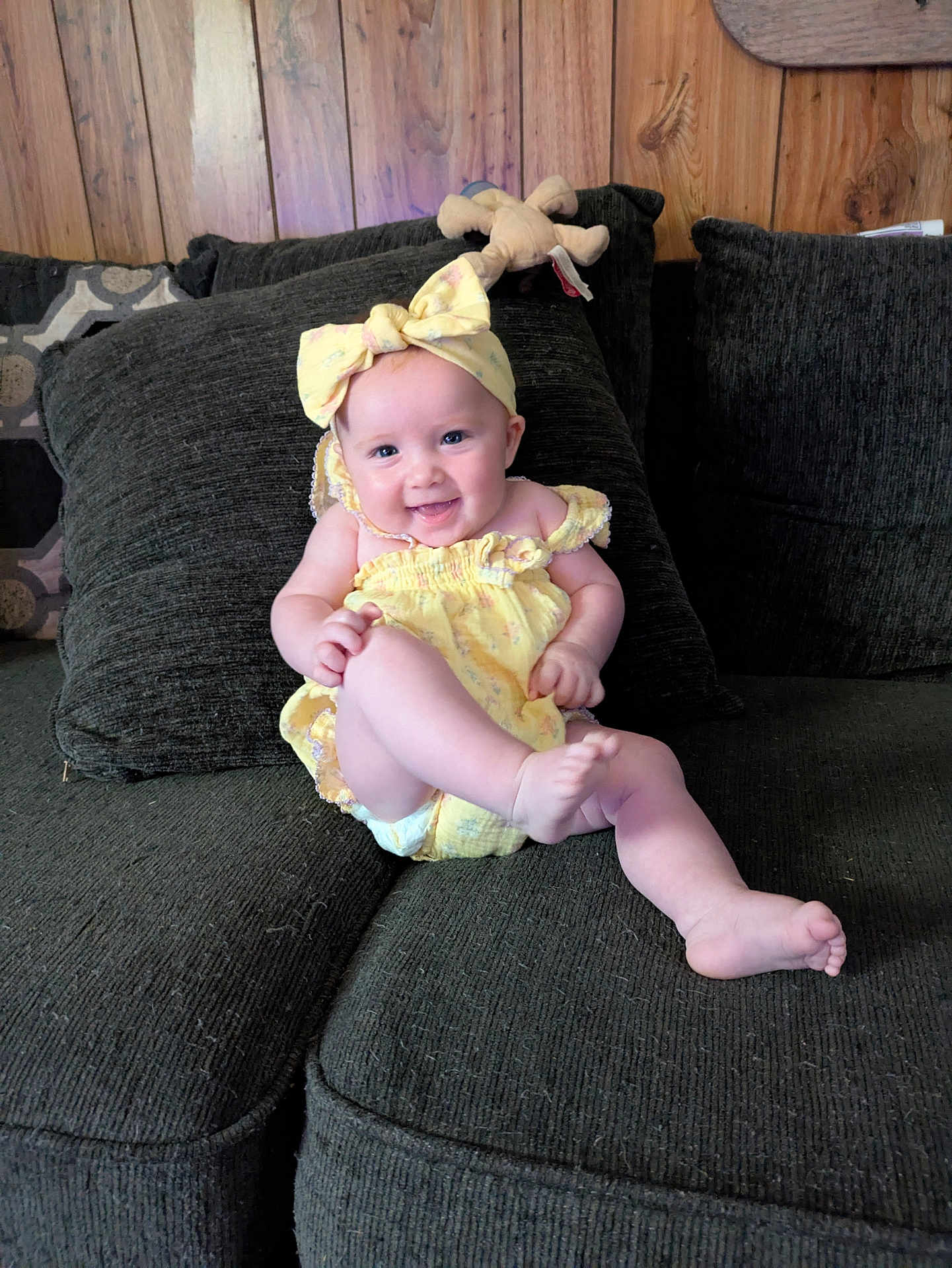 Lilith Fae Deatley joined the competition — help win amazing prizes! baby, smiling, yellow_outfit, headband, couch, plush_toy, wood_paneling, happy, infant, child, indoors, cute, sitting, person, furniture, cheerful, playful, young_child, cozy, portrait