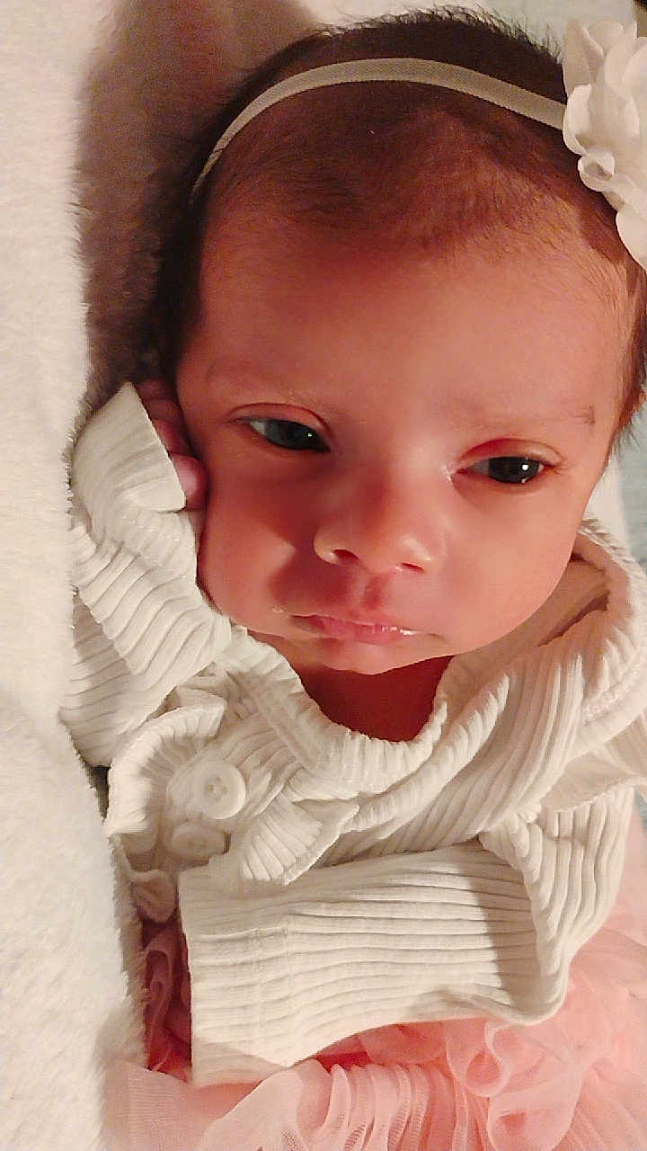 Azrael joined the competition — help win amazing prizes! baby, infant, face, headband, flower, white_sweater, pink_skirt, blanket, resting, portrait, closeup, cute, soft_texture, newborn, child, young, sleepy, cozy, indoors, peaceful