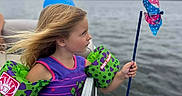 Maeve is registered to the contest to win money with this photo: child, clothing, face, female, flag, girl, head, lake, lifejacket, nature, outdoors, person, photography, portrait, summer, swimwear, transportation, vest, water, waterfront