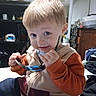 Raiden joined the competition — help win amazing prizes! blond_hair, blue_eyes, boy, candid, child, close_up, eating, facial_expression, happy, home, indoor, kitchen, orange_sweater, portrait, seated, smiling, spoon, toddler, utensil, vest