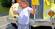 Raiden joined the competition — help win amazing prizes! child, chrome, front_grille, gray_pants, happy, hat, headlight, outdoors, playful, portrait, road, smiling, sunlight, toddler, toy, trees, vehicle, vintage_truck, white_shirt, yellow_vehicle