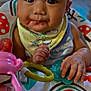 Hennessey is registered to the contest to win money with this photo: baby, child, face, bib, bow, toy, hand, feeding, messy, expression, colorful, pattern, indoor, closeup, infant, cute, happy, playtime, seat, food
