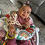 Hennessey is registered to the contest to win money with this photo: baby, infant, child, pink_bow, baby_walker, toy, colorful, rainbow_pattern, floral_clothing, pink_pants, indoor, carpet, couch, wooden_floor, hand, face, smile, curious, seated, cozy