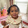 toddler, child, smiling, indoor, window_blinds, lotion_bottle, hairbrush, marble_surface, cheeky_smile, wet_hair, clothing, cherry_pattern, diaper, bracelet, natural_light, face, person, cute, baby, sitting