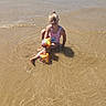 Jade a rejoint le concours — aidez-le/la à gagner de superbes lots ! child, girl, beach, water, swimsuit, floaties, sand, sunlight, smile, summer, outdoor, vacation, shallow_water, happy, sitting, glasses, hair_tied_up, playful, fun, sunny