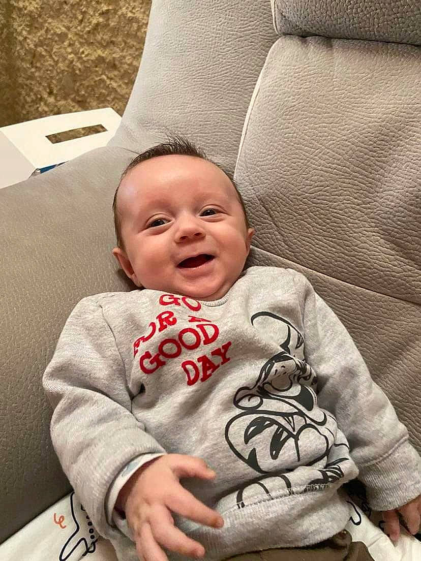 Gino a rejoint le concours — aidez-le/la à gagner de superbes lots ! baby, baby_toddler_clothing, chair, cheek, chin, comfort, couch, face, grey, happy, head, linens, person, sitting, skin, sleeve, smile, t_shirt, textile, toddler