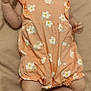 baby, infant, child, romper, headband, floral_pattern, peach_color, lying_down, blanket, cute, chubby, skin, person, young, indoors, expression, clothing, feet, arms, legs