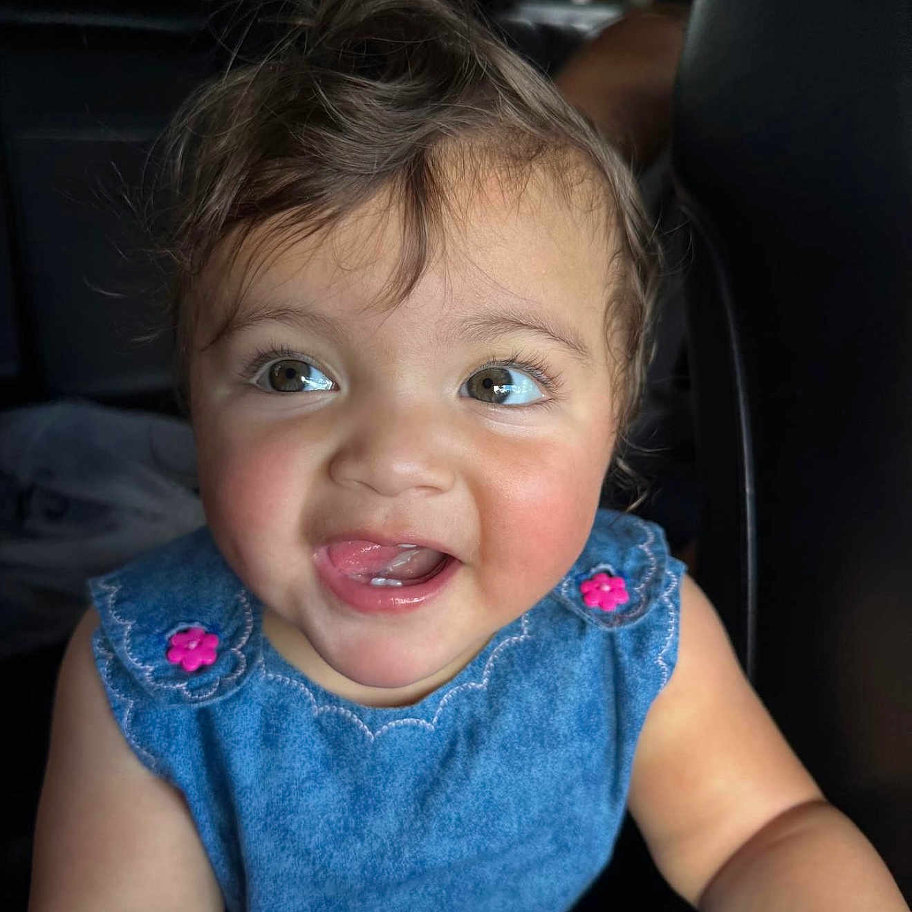 Daniela is registered to the contest to win money with this photo: arm, baby, blue_dress, car_seat, cheeks, child, cute, eyes, face, hair, happy, infant, inside_car, mouth_open, natural_light, pink_buttons, portrait, skin, smiling, toddler