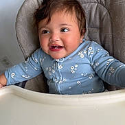 Daniela joined the competition — help win amazing prizes! baby, child, high_chair, blue_clothing, floral_pattern, smiling, happy, indoor, face, person, young_child, cute, kitchen, utensil_pattern, seat, infant, table, portrait, sitting, cheerful