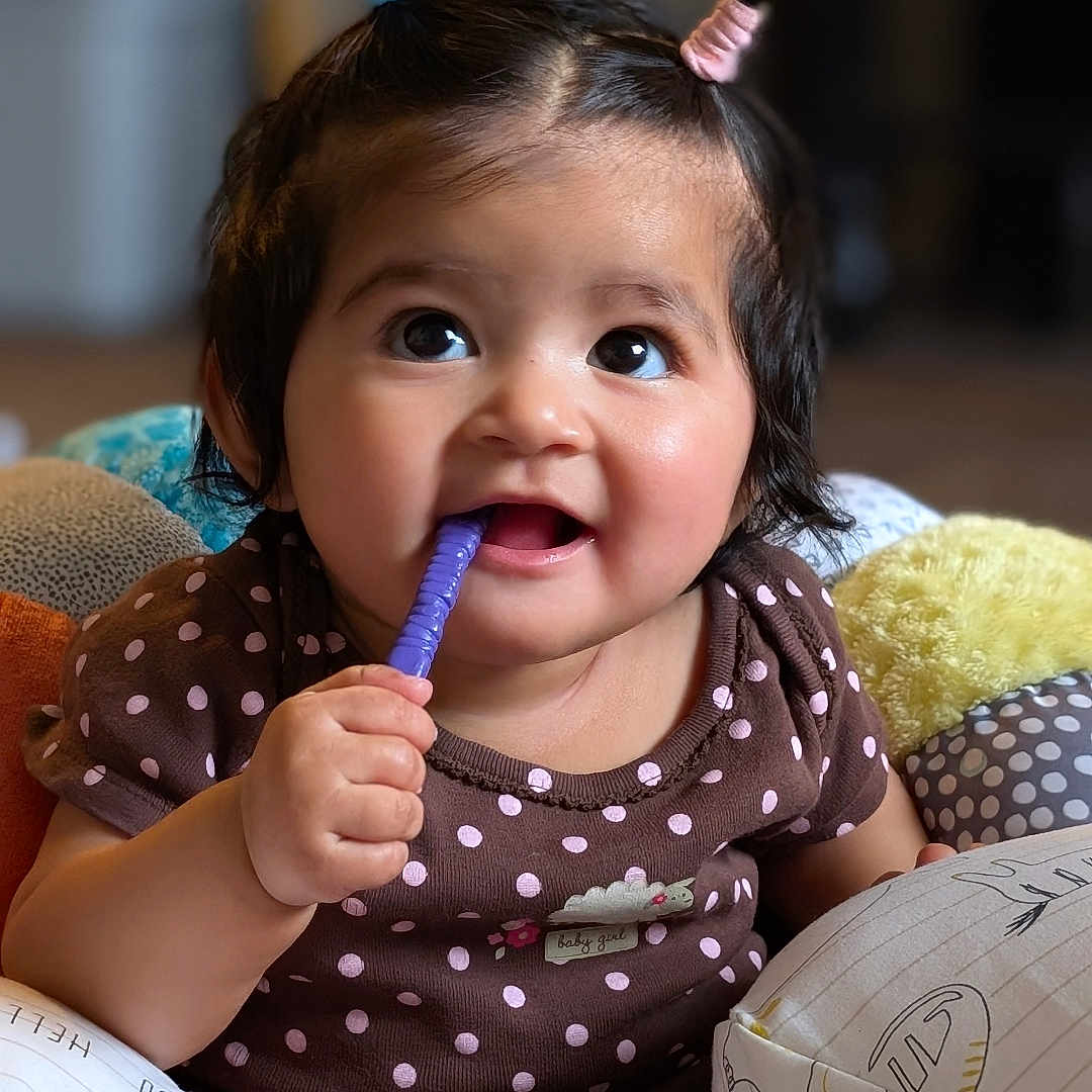Sparsha is registered to the contest to win money with this photo: baby, brown_clothing, child, cushion, cute, face, foot, hand, happy, indoors, infant, pigtails, playful, polka_dot, portrait, purple, sitting, smiling, toddler, toy