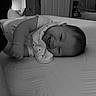 baby, infant, sleeping, bed, bedroom, blanket, onesie, portrait, face, closed_eyes, curled_up, lying_down, indoors, home, furniture, bedding, monochrome, black_and_white, peaceful, child