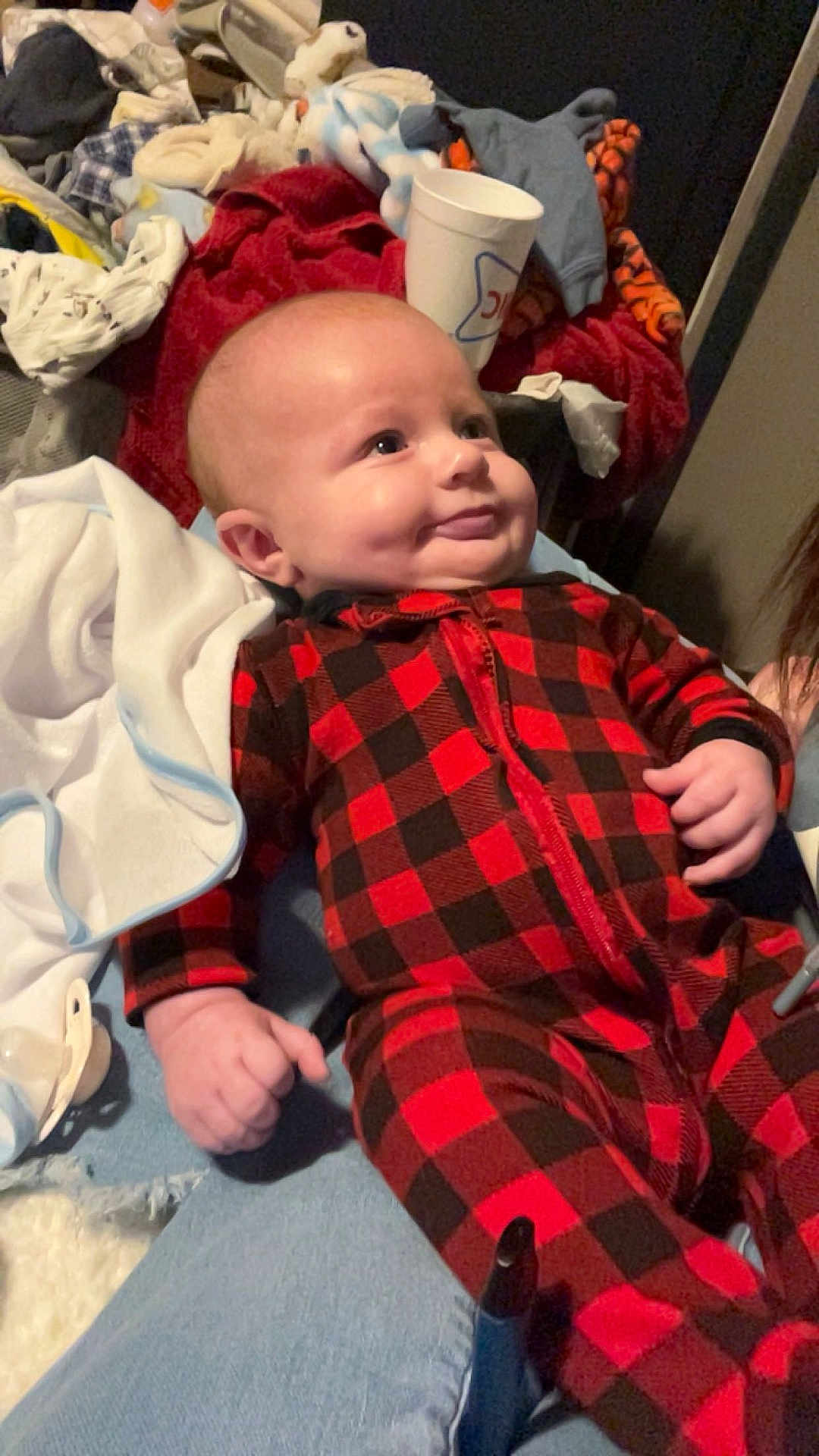 Hayes joined the competition — help win amazing prizes! baby, infant, plaid_pajamas, red_black_pattern, dimple, smile, laying_down, blanket, bedding, laundry_pile, cup, pacifier, hand, onesie, portrait, indoors, cozy, soft_toys, cloth, person