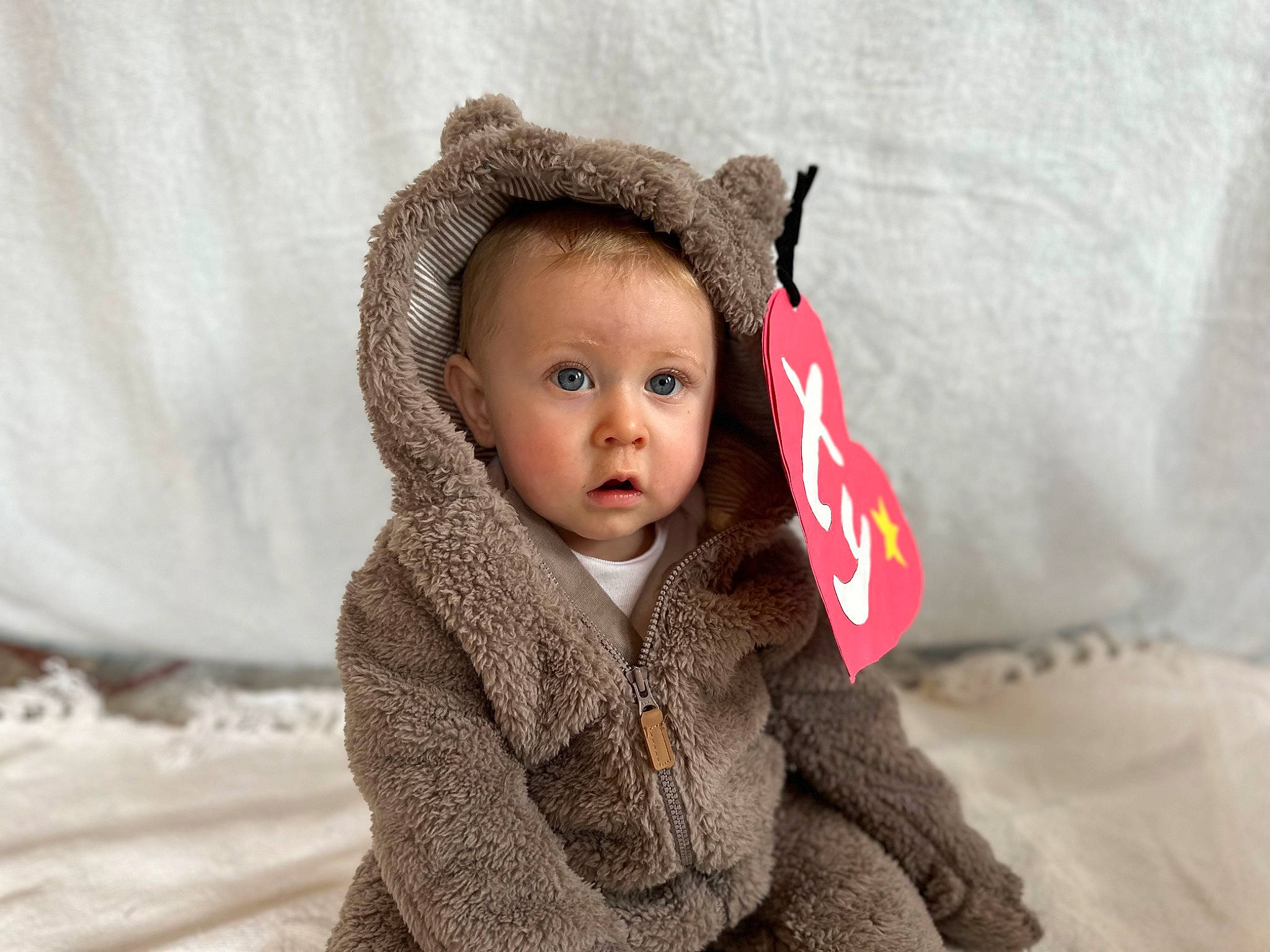 Logan joined the competition — help win amazing prizes! baby, baby_toddler_clothing, cap, cheek, child, comfort, eye, fashion_accessory, fur, happy, head, hood, linens, person, polar_fleece, portrait_photography, sitting, sleeve, surprise, toddler
