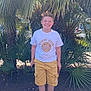 boy, casual_clothing, child, daylight, footwear, greenery, happy, leisure, nature, outdoor, palm_tree, portrait, sandals, shorts, smiling, standing, summer, sunny, tshirt, youth