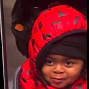 Lycia participe au concours pour gagner de l'argent avec cette photo : child, face, hood, jacket, red, black, smile, indoor, clothing, young, person, cute, warm, peeking, portrait, expression, winterwear, seated, hoodie, playful