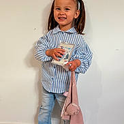 Layana a rejoint le concours — aidez-le/la à gagner de superbes lots ! child, girl, pigtails, blue_bows, striped_shirt, jeans, white_shoes, smile, standing, indoor, plush_toy, book, happy, cute, person, portrait, young_child, floor, wooden_floor, wall