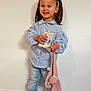 child, girl, pigtails, blue_bows, striped_shirt, jeans, white_shoes, smile, standing, indoor, plush_toy, book, happy, cute, person, portrait, young_child, floor, wooden_floor, wall