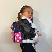 Layana participe au concours pour gagner de l'argent avec cette photo : accessory, backpack, black_jacket, child, clothing, cute, fashion, girl, happy, indoor, pacifier, pigtails, plush_toy, polka_dot, portrait, smile, standing, white_fur, wooden_floor, young_child