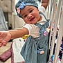 baby, child, smiling, blue_dress, flower, hat, crib, blanket, indoor, happy, person, cute, toddler, playful, clothing, furniture, soft_toys, floor, home, portrait
