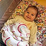 baby, blanket, playpen, smile, infant, floral_pattern, cozy_clothing, pacifier, mittens, cute, child, comfort, indoors, soft_texture, happy, portrait, lying_down, colorful, warm, young