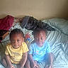 Elijah'Nae is registered to the contest to win money with this photo: child, toddler, bed, pillow, toy, yellow_shirt, blue_shirt, socks, indoors, curly_hair, cute, sitting, blanket, furniture, person, home, casual_clothing, playful, young, portrait