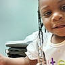 Elijah'Nae joined the competition — help win amazing prizes! child, smiling, close_up, braids, beads, shirt, arm, medical_table, indoor, person, face, young_child, curious, playful, healthcare, clinic, examination_room, light_skin, happy, casual_clothing