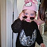 toddler, child, blue_eyes, pink_beanie, hello_kitty, sunglasses, black_sweater, sequins, wings, indoor, person, hand, floor, doorframe, jeans, cute, fashion, young_child, portrait, casual