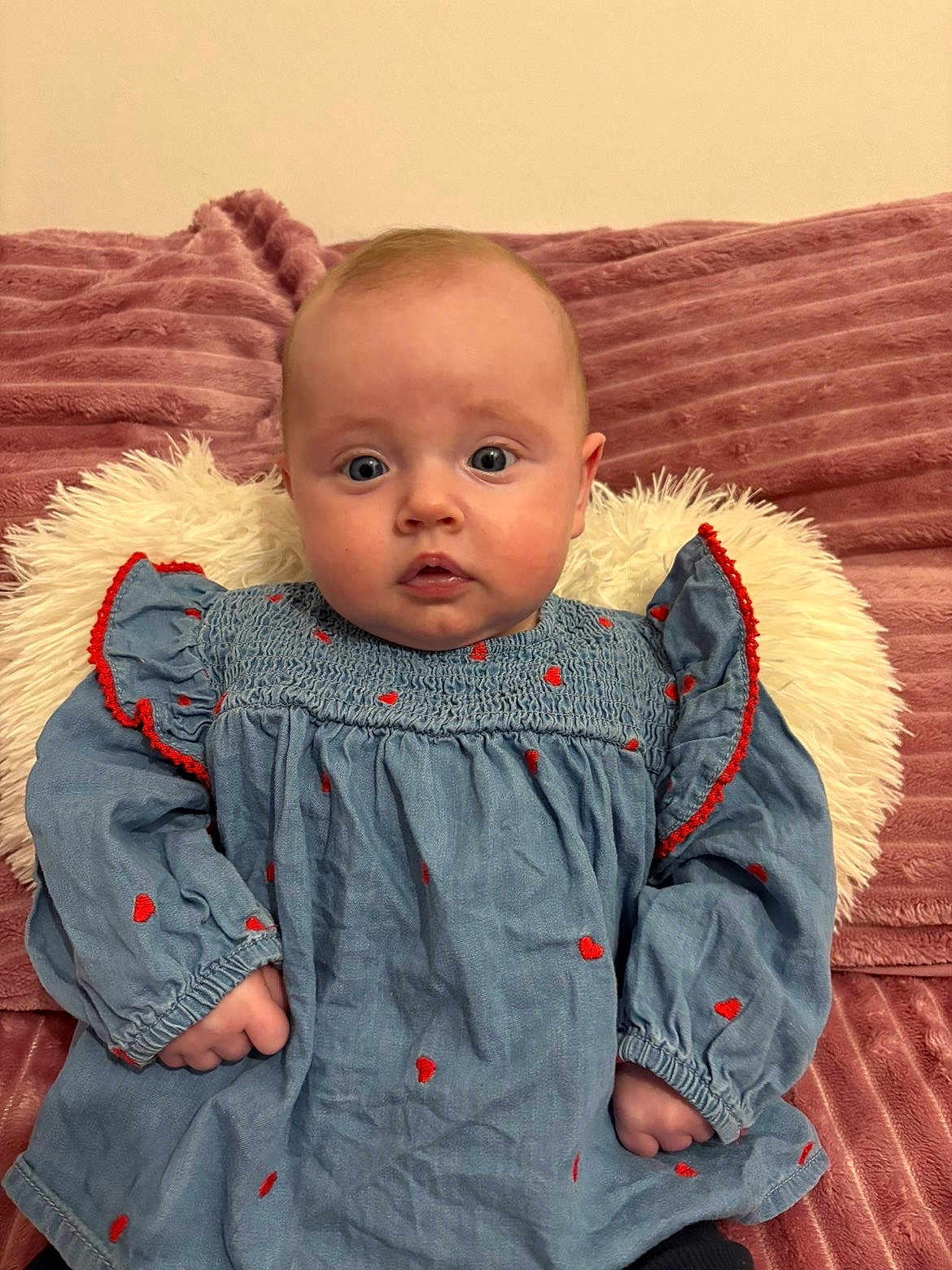 Jeanna a rejoint le concours — aidez-le/la à gagner de superbes lots ! baby, infant, child, portrait, blue_dress, red_hearts, fluffy_pillow, pink_blanket, sofa, wide_eyes, surprised_expression, hands, sitting, indoor, cute, face, plush_texture, home, skin, young_baby