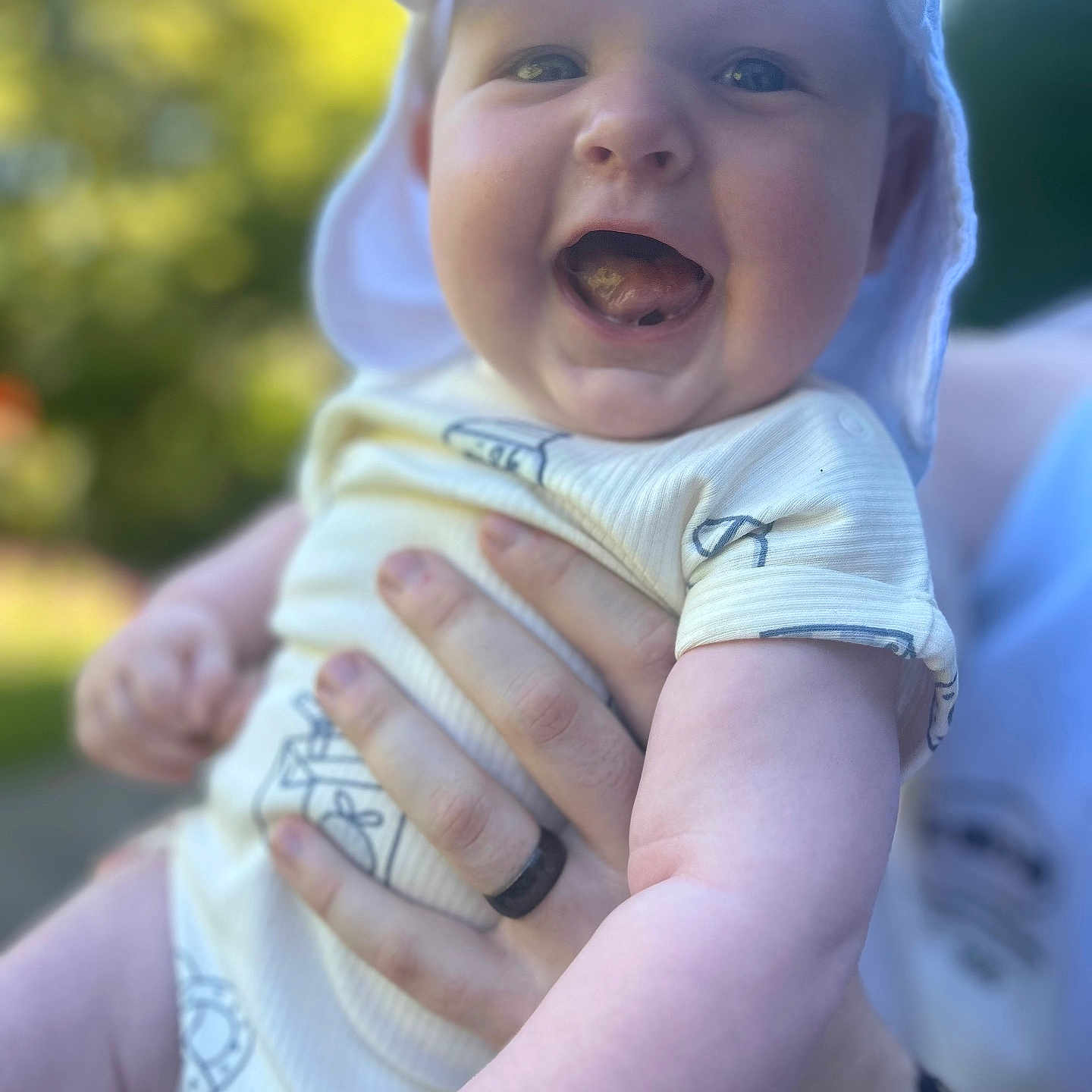 Kraven joined the competition — help win amazing prizes! adult, baby, blurred_background, child, cute, face, greenery, hand, happy, hat, holding, nature, onesie, outdoor, person, portrait, skin, smiling, sunlight, tongue