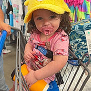 Marie joined the competition — help win amazing prizes! toddler, child, shopping_cart, hat, yellow_hat, pacifier, pink_clothing, curly_hair, store, clothing_rack, colorful_clothes, orange_cup, baby, footwear, person, retail, shopping, cute, indoor, casual