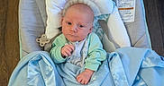 Owen is registered to the contest to win money with this photo: baby, infant, blanket, blue_blanket, baby_seat, cushion, wooden_floor, clothing, face, person, indoor, newborn, child, sitting, soft_texture, pacifier_clip, head_support, looking_at_camera, small_fist, cozy